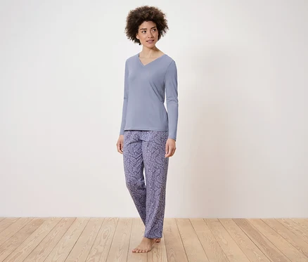 Une femme debout porte un pyjama bleu à manches longues et un pantalon à motifs.
