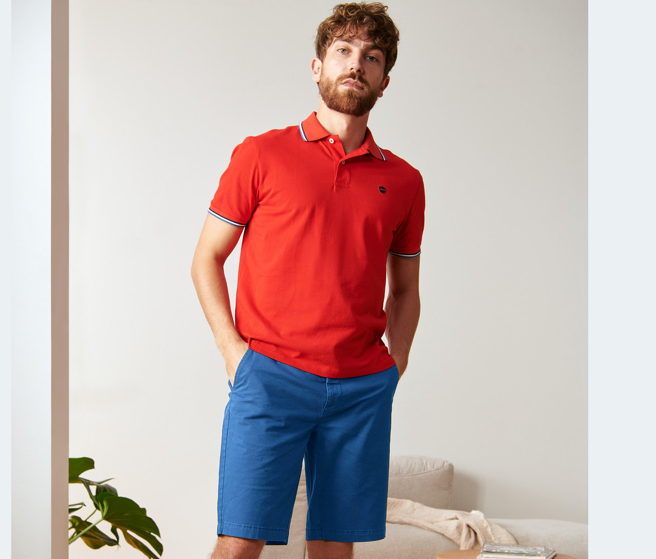 Un homme pose en polo rouge et short chino bleu roi.
