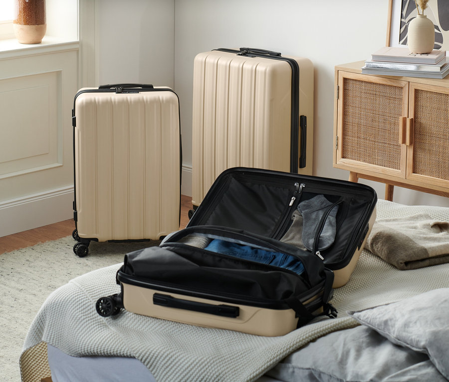 Trois valises rigides recyclées beiges sont posées dans la pièce, dont une ouverte sur le lit.