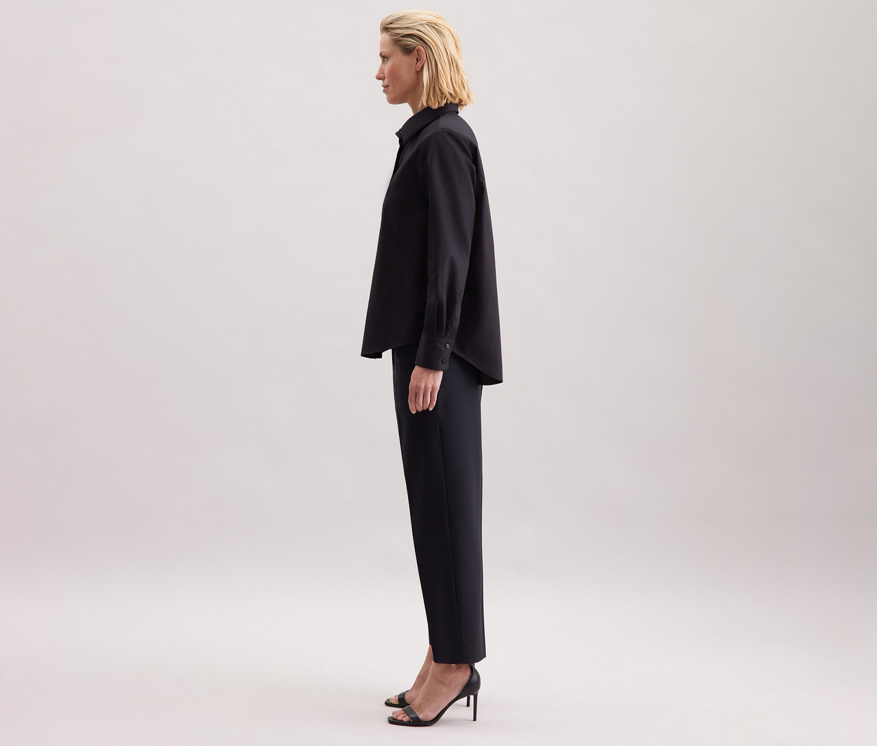 Une femme porte un chemisier noir Seidensticker de coupe régulière, un pantalon noir et des chaussures à talons hauts.