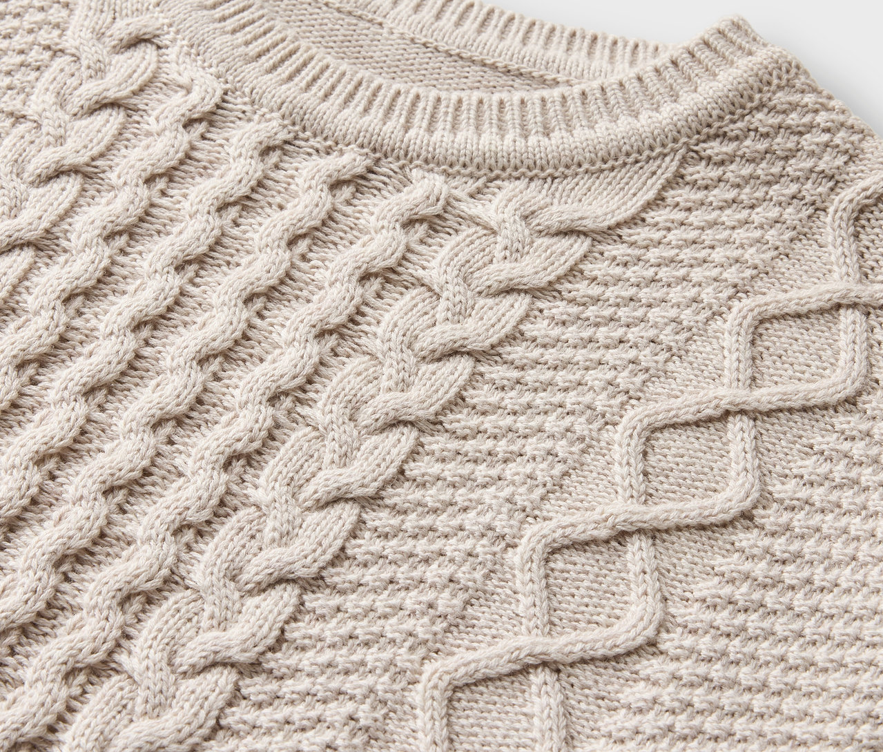 Gros plan d'un pull en tricot crème avec motif torsadé.