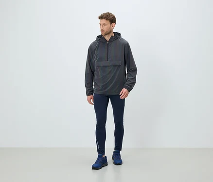 Un homme debout portant un coupe-vent gris à capuche, des leggings bleu marine et des chaussures bleues.