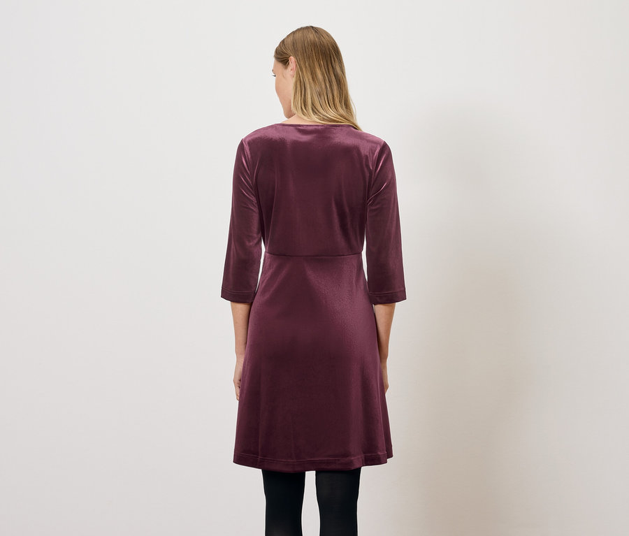 Une femme se tient dos à la caméra et porte une robe en velours bordeaux à manches trois-quarts.