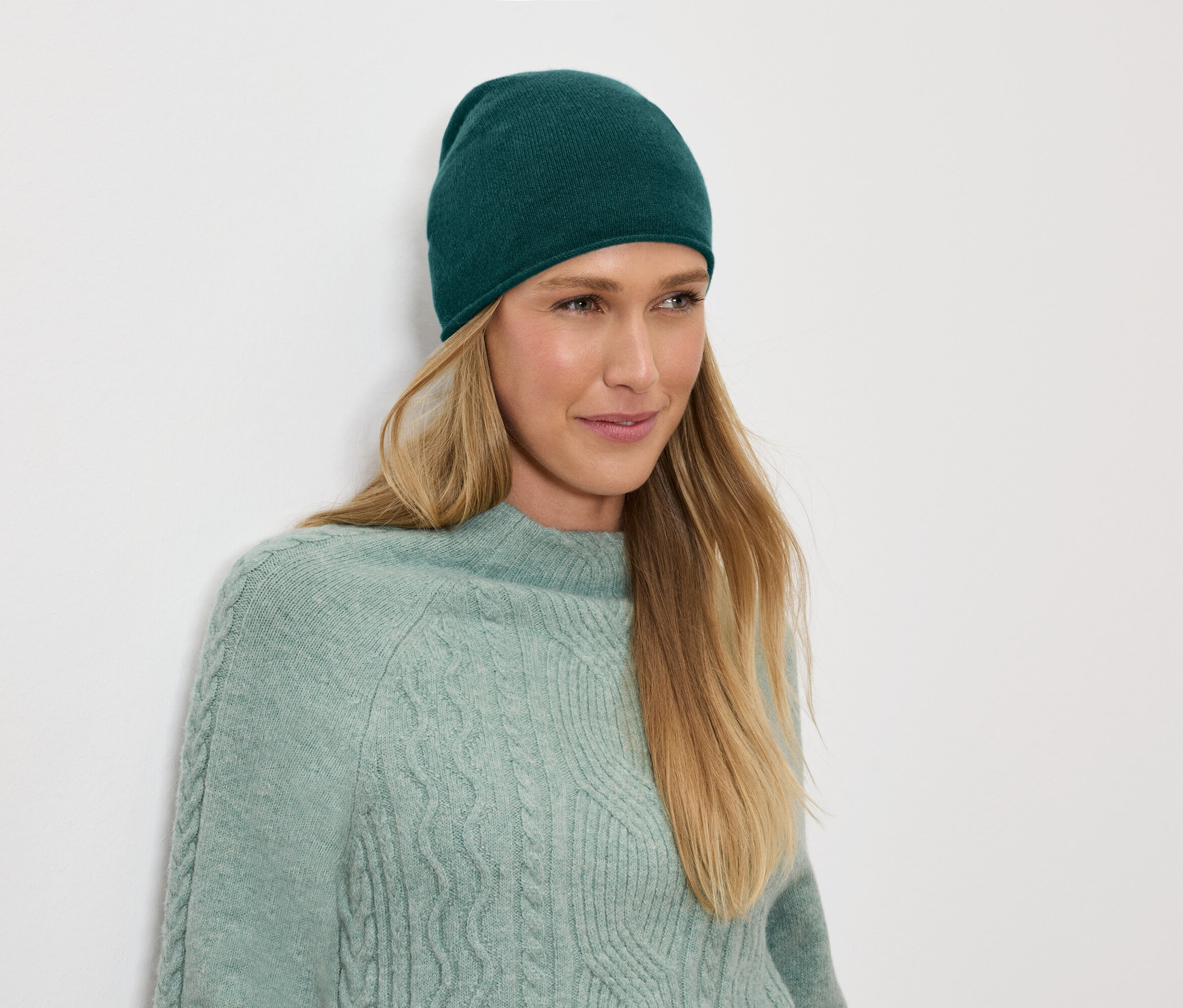 Une femme aux cheveux blonds porte un bonnet vert et un pull.
