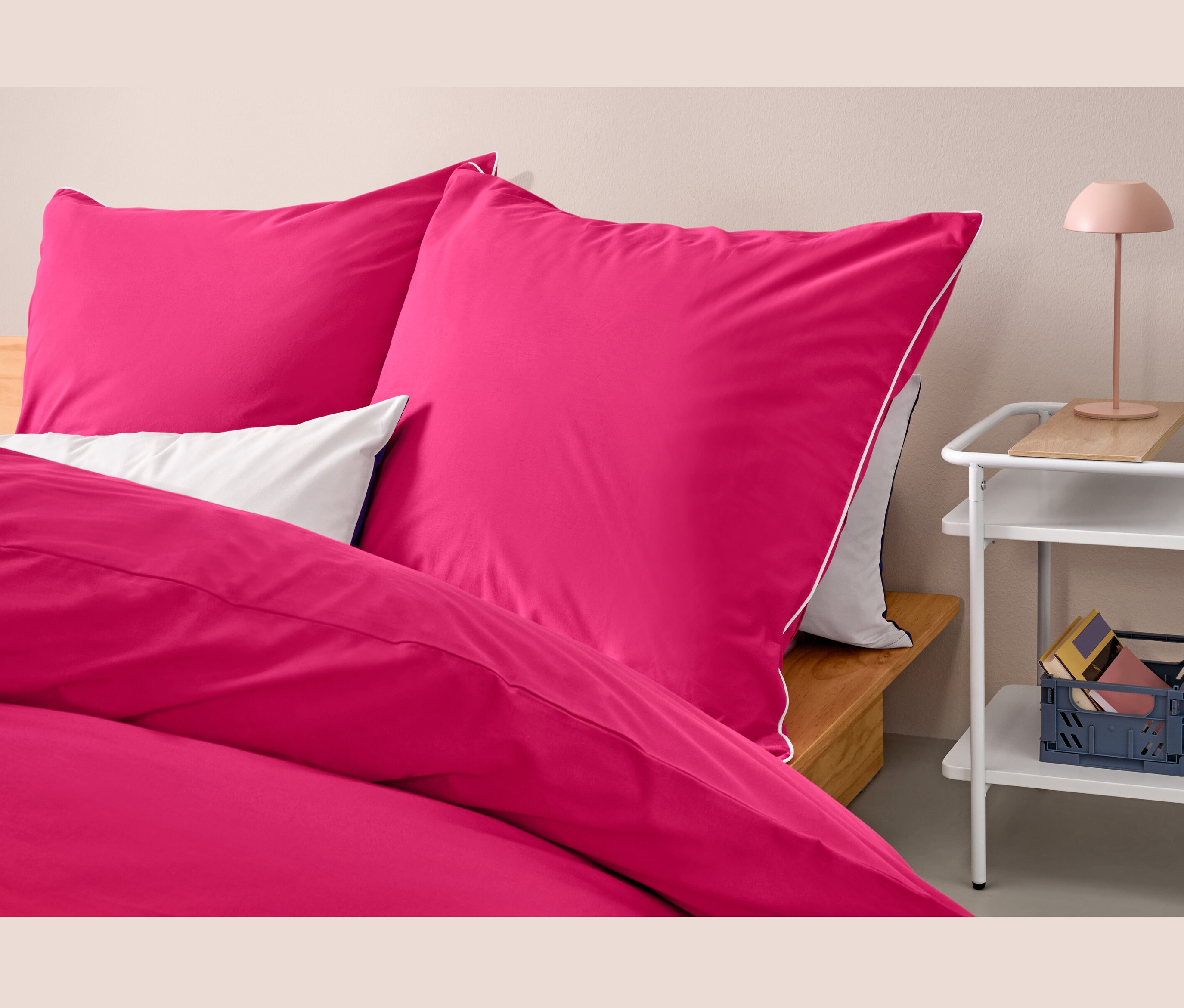 Gros plan de trois ensembles de parure de lit rose en renforcé de taille standard sur un lit à côté d'une table.