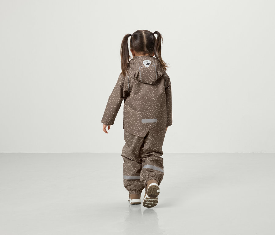 Fillette avec des couettes marchant sur le sol dans une veste et un pantalon à capuche marron.