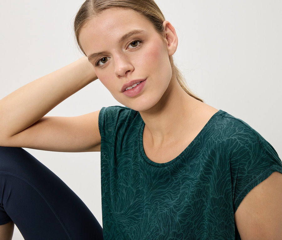 Une femme est assise et porte un t-shirt vert à motifs et un legging bleu.