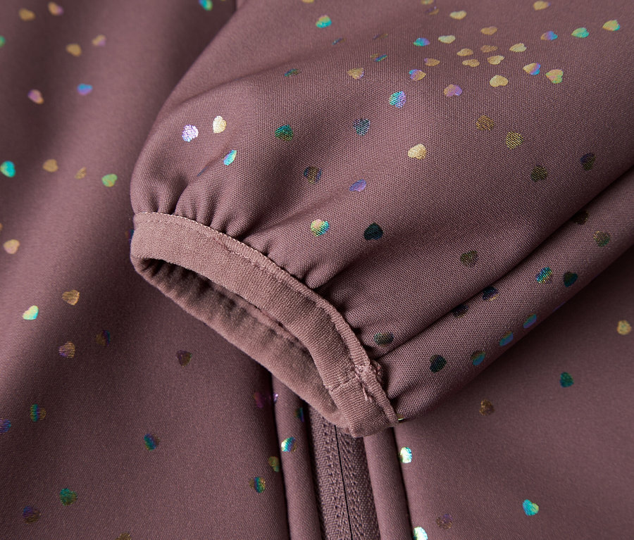 Gros plan sur la manche et la fermeture éclair d'une veste softshell violette avec des petits cœurs colorés.