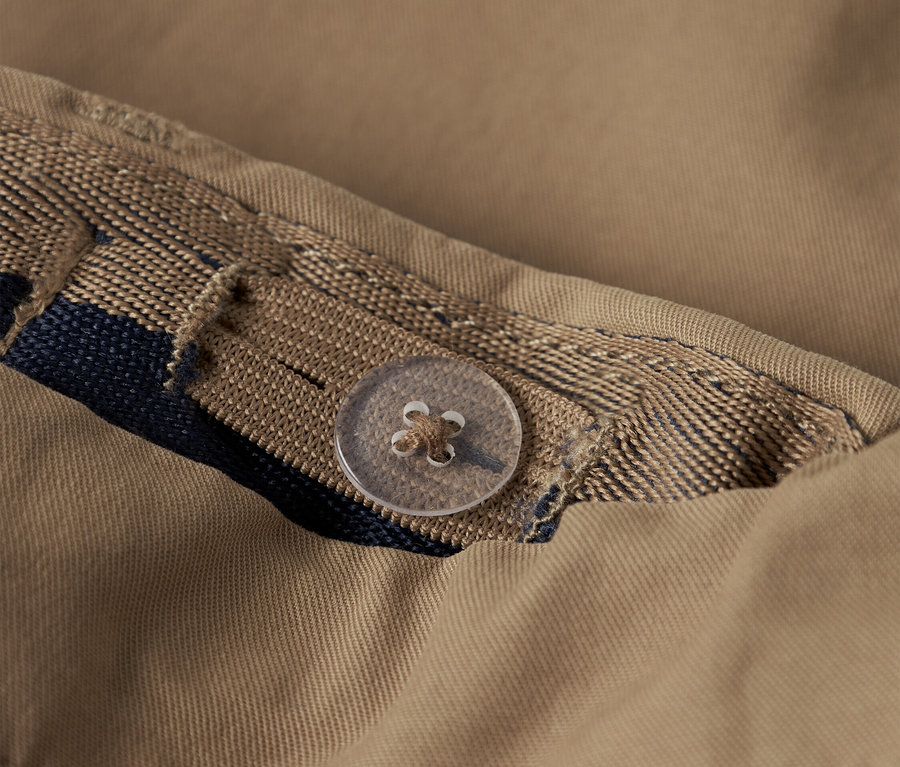 Gros plan d'une chemise beige avec un bouton et un ruban décoratif.