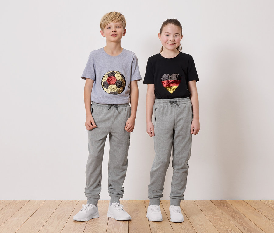 Un garçon portant un t-shirt gris avec un motif de ballon de football et une fille portant un t-shirt noir avec un motif de cœur, tous deux portant des pantalons de survêtement gris.
