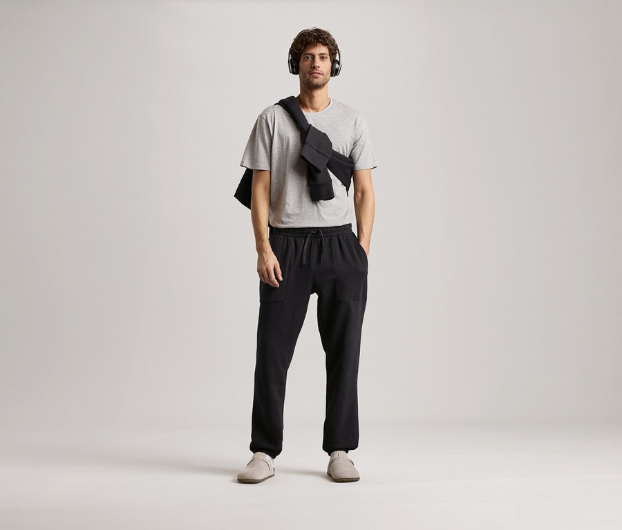 Homme portant des écouteurs, un t-shirt gris et un pantalon de survêtement noir.