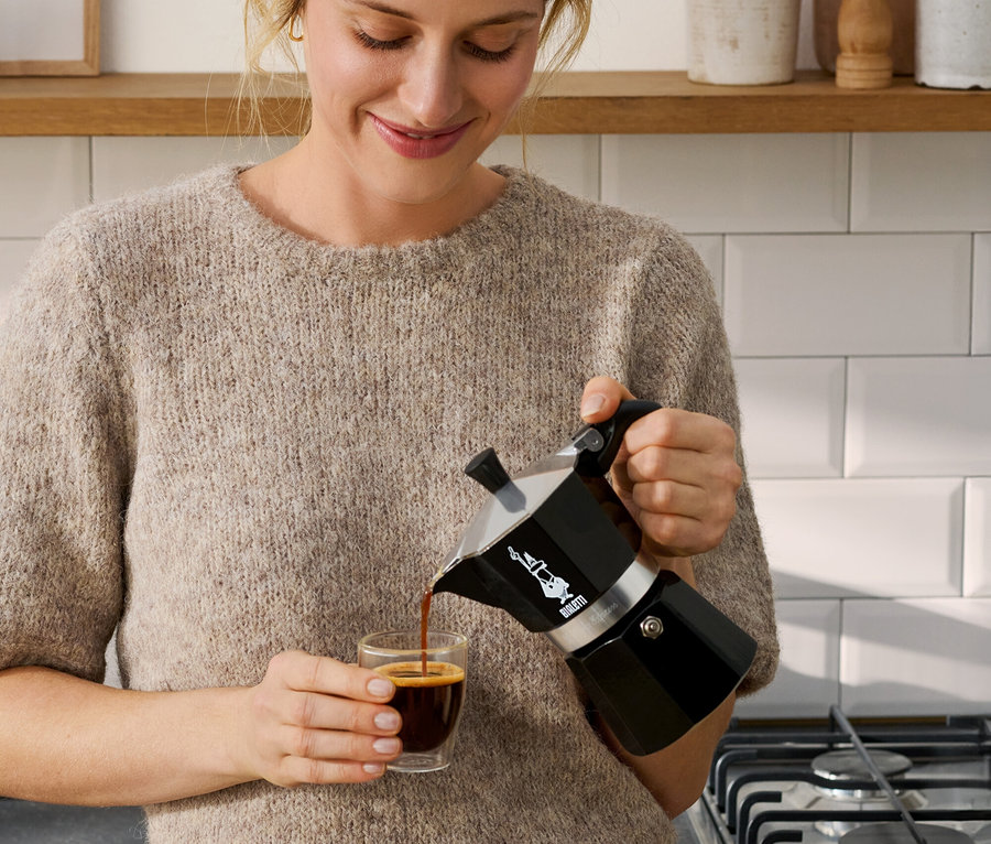 Femme versant du café d'une cafetière Bialetti Moka Express noire, 190 ml, dans une tasse.