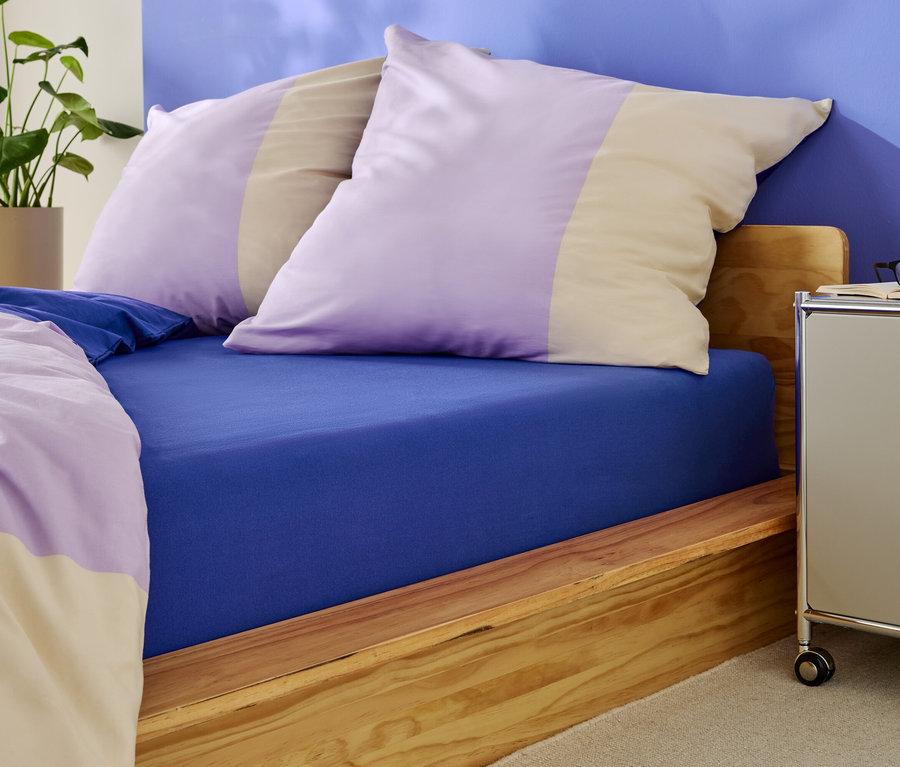 Lit avec drap-housse bleu et oreillers à rayures violettes et beiges.