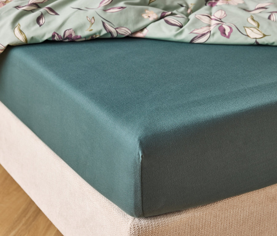 Gros plan d'un matelas vert foncé avec un drap-housse vert menthe à motifs floraux sur le dessus.