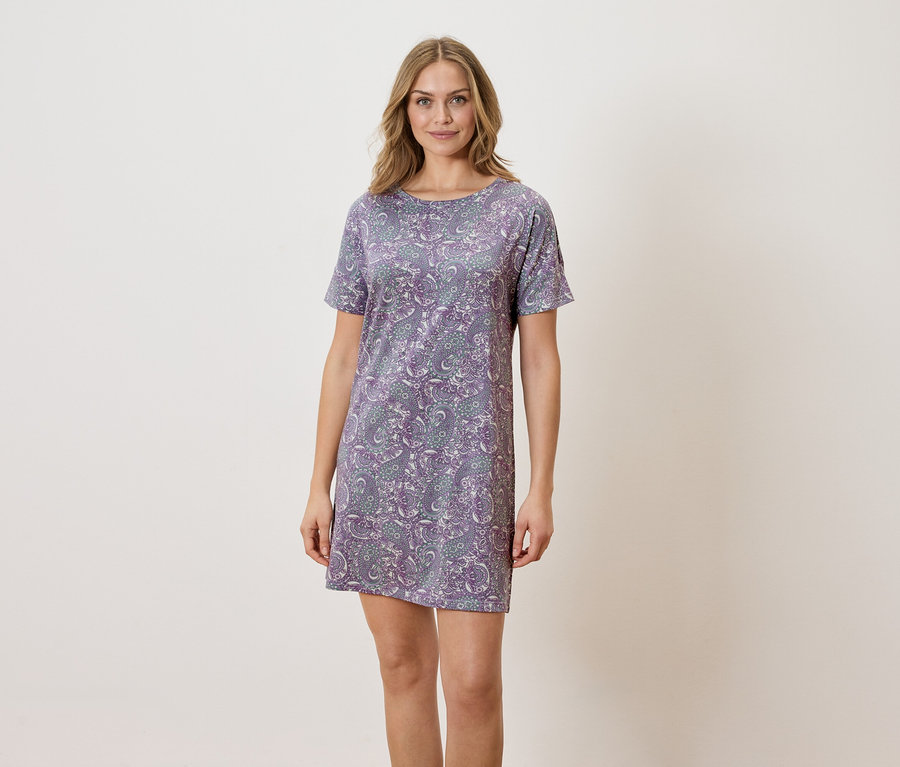Femme debout portant une robe violette à motifs floraux.