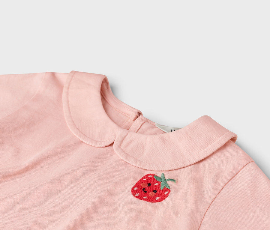Vue détaillée d'une robe rose clair avec un motif de fraise brodé et un col Claudine.
