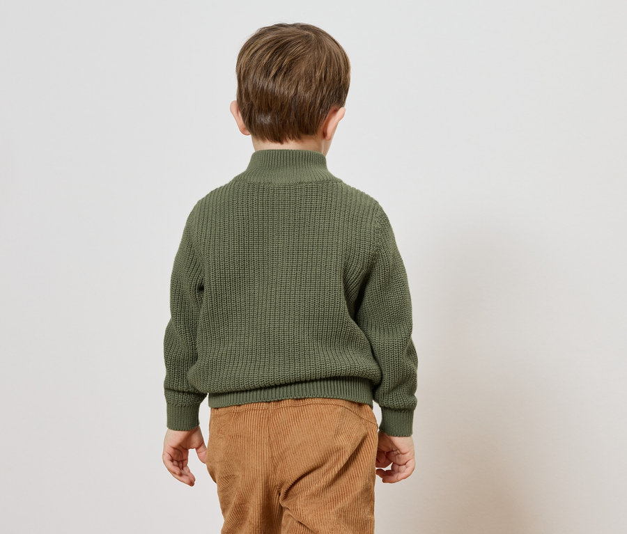 Vue de dos d'un enfant aux cheveux bruns portant un pull en tricot vert olive et un pantalon en velours côtelé marron.