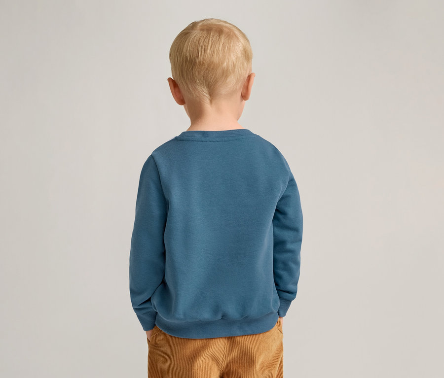 Vue arrière d'un enfant blond portant un sweat-shirt bleu et un pantalon en velours côtelé marron.