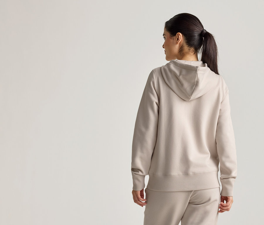 Vue arrière d'une femme avec une queue de cheval portant un sweat à capuche beige et un pantalon assorti.