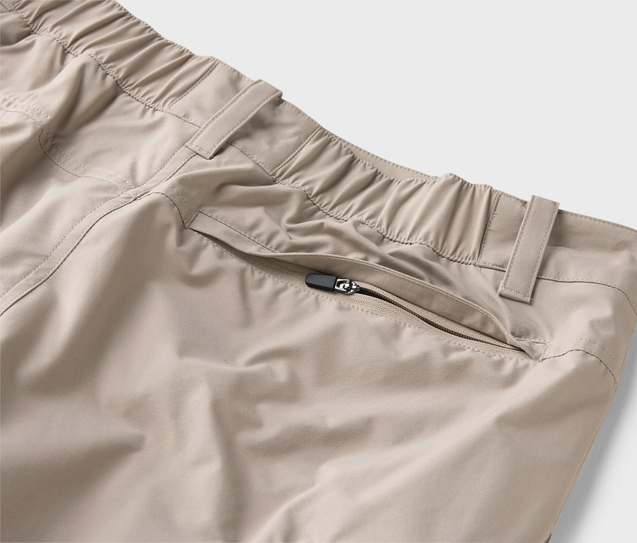 Gros plan d'un pantalon beige avec une taille élastique et une poche zippée.