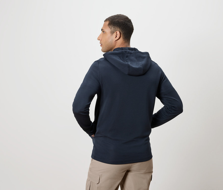 Homme vu de dos portant un sweat à capuche bleu marine et un pantalon beige, les mains dans les poches.