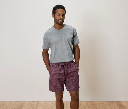 Un homme se tient debout, les mains dans les poches, portant un pantalon gris et un short à motifs.