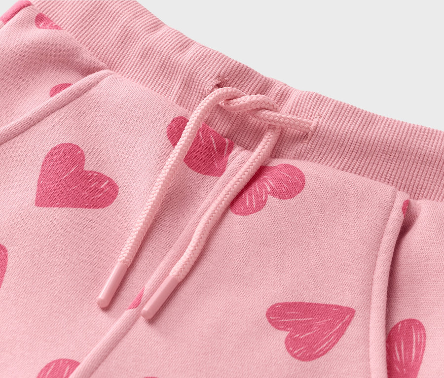 Gros plan d'un pantalon de survêtement rose clair avec un motif de cœur rose foncé et un cordon de serrage.