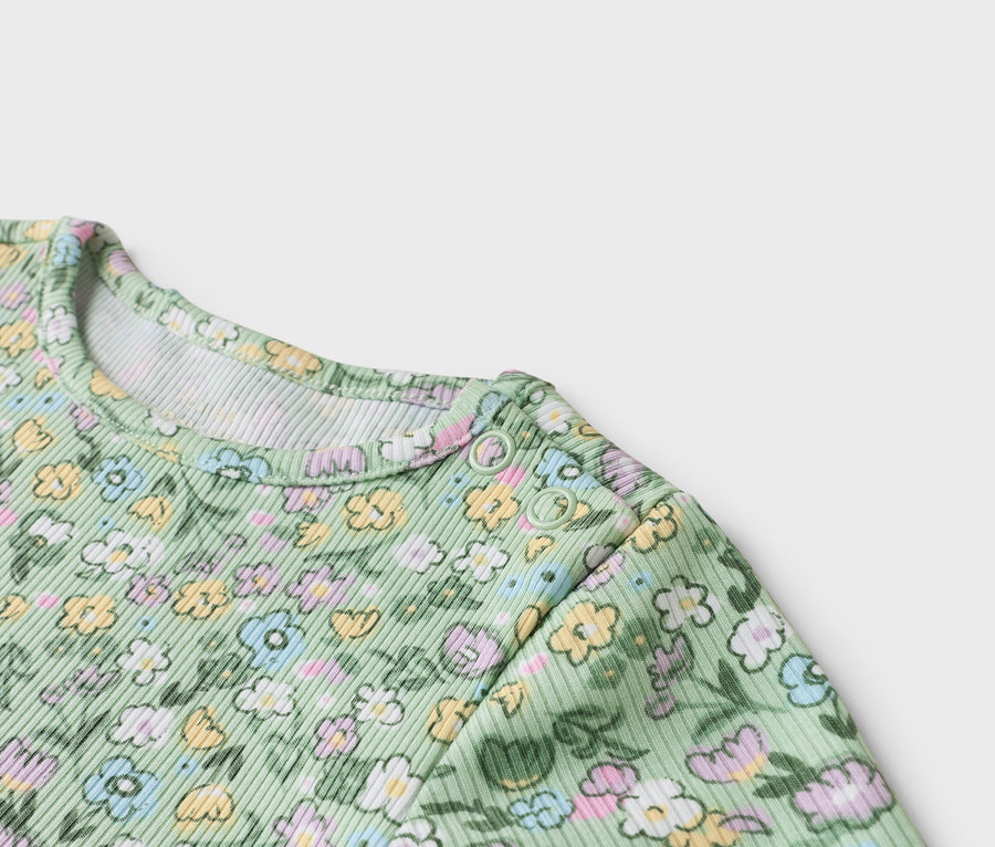 Gros plan sur un body bébé vert clair à motif floral avec boutons-pression à l'épaule.