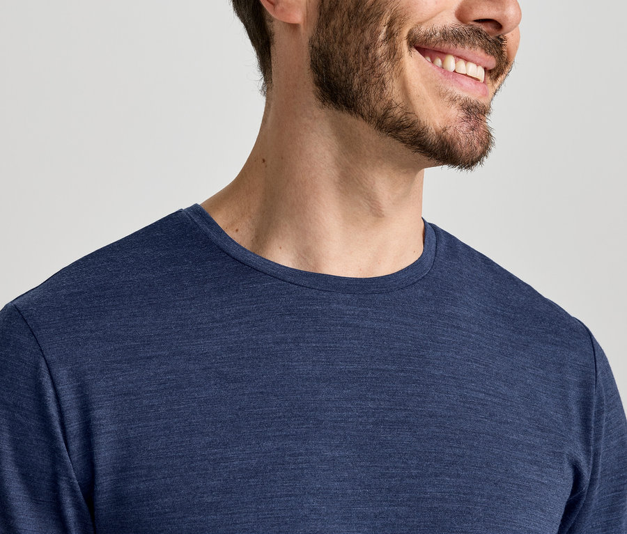 Gros plan d'un homme souriant avec une barbe, portant un t-shirt bleu à manches longues.