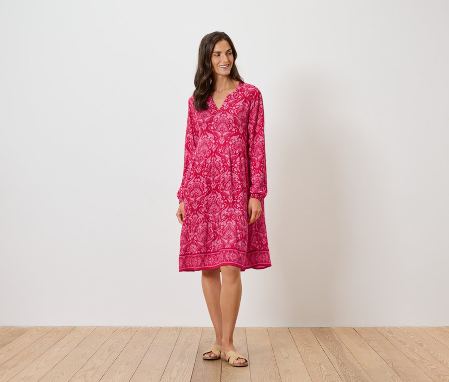 Femme debout portant une robe rose à motifs à manches longues et des sandales.