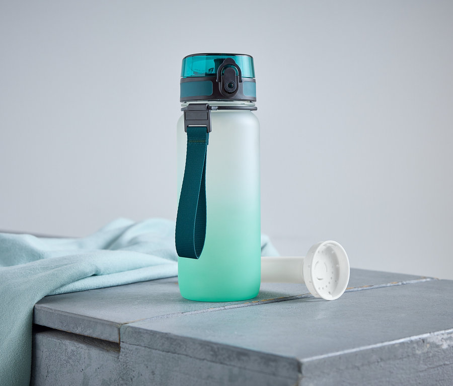 Une bouteille d'eau avec un bouchon et une lanière turquoise est posée sur une surface grise à côté d'un tissu bleu clair.