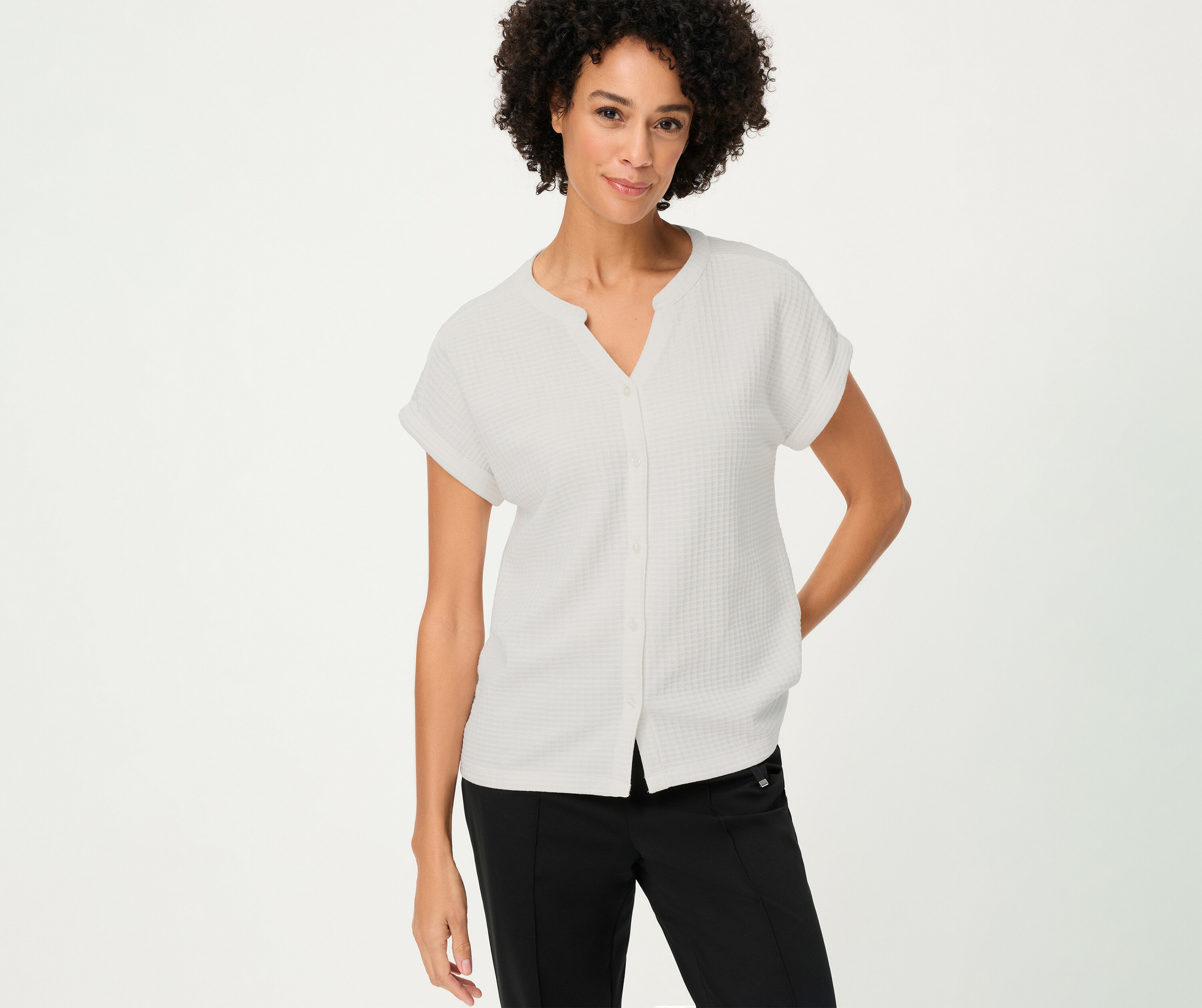 Une femme aux cheveux bouclés porte un t-shirt Olsen structuré avec boutons blanc et un pantalon noir.