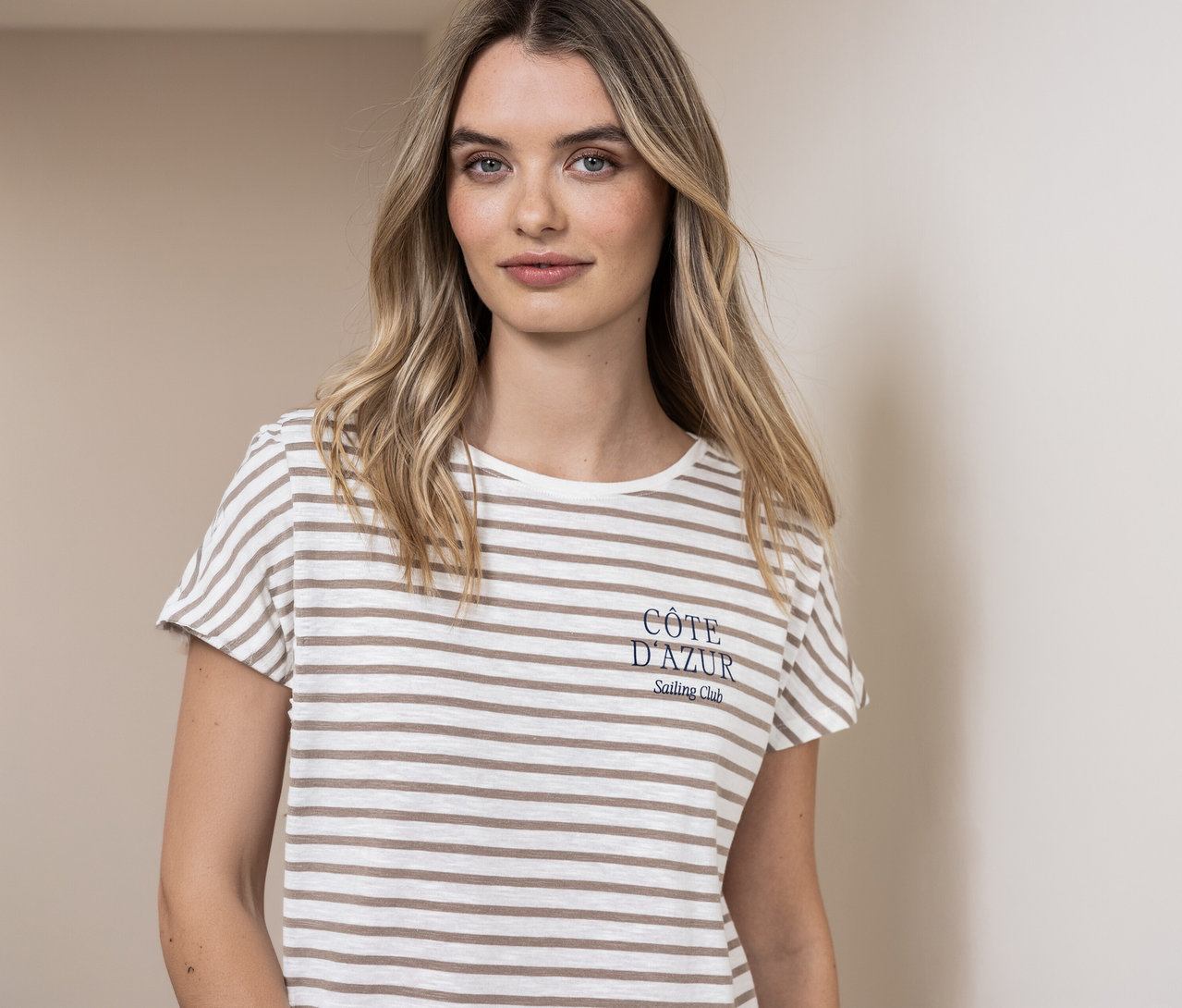Une femme porte un t-shirt Street One beige et blanc rayé avec l'inscription « Côte d'Azur ».