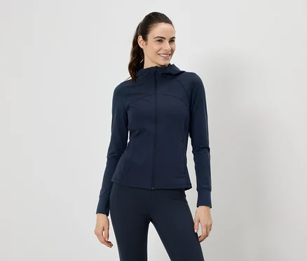 Une femme souriante portant une veste à capuche bleu marine et un legging, les cheveux attachés en queue de cheval.