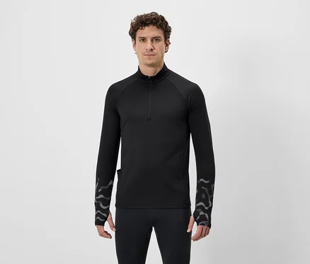 Un homme aux cheveux bouclés porte un t-shirt noir à manches longues avec fermeture éclair et un legging sur fond blanc.