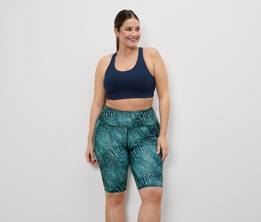 Femme portant un soutien-gorge de sport bleu marine et un cycliste vert à motifs sur fond blanc.