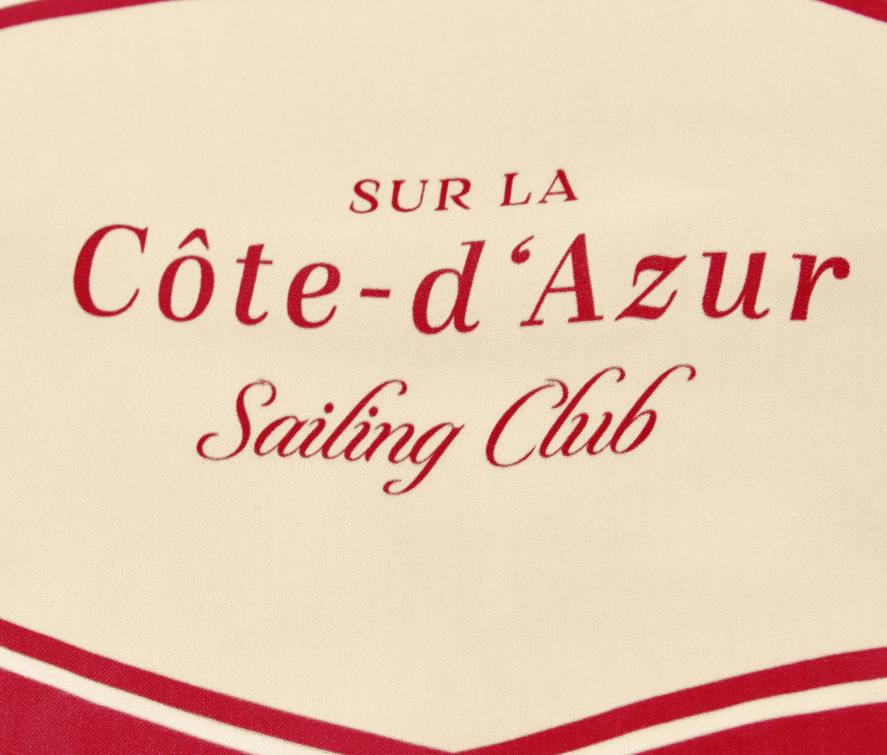 Gros plan du foulard Street One « Nicki » avec l'inscription rouge « Côte-d'Azur Sailing Club » sur fond beige.