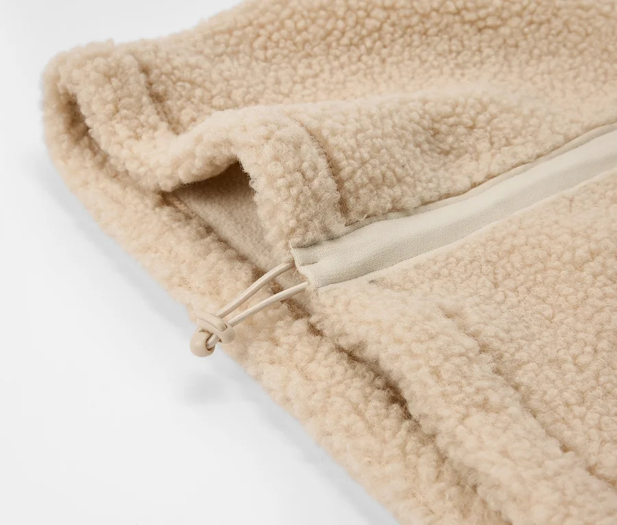 Gros plan d'un Teddy-Schlauchschal beige à la texture moelleuse, avec un cordon de serrage et un stoppeur visibles.