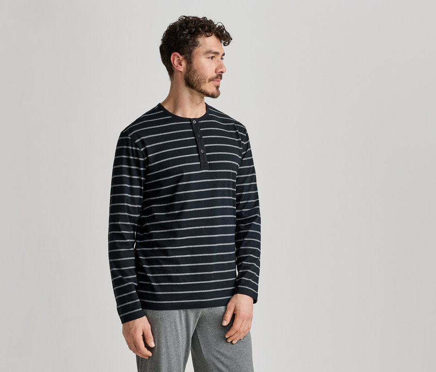 Homme portant un haut rayé à manches longues et un pantalon gris, de profil sur fond clair.