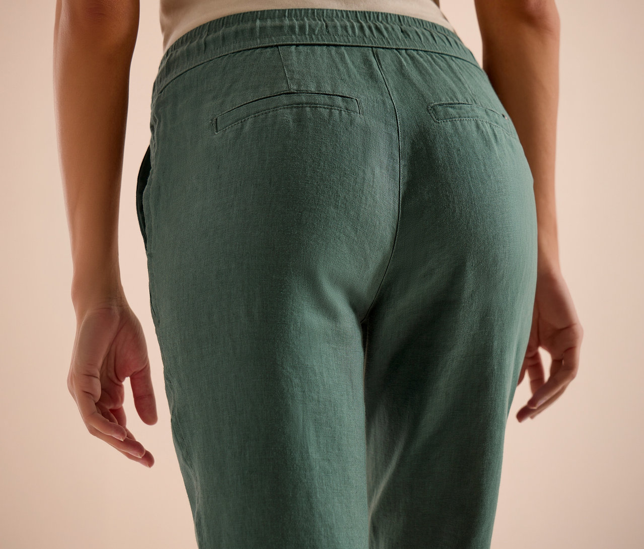 Vue arrière d'une personne portant un pantalon en lin vert avec une taille élastique et des poches arrière.