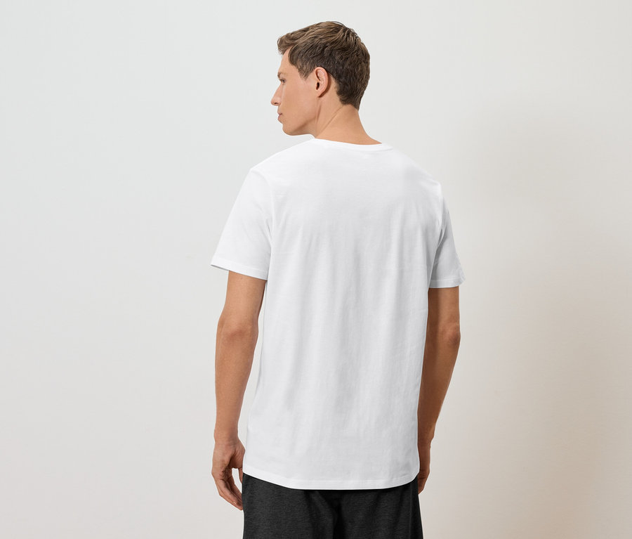 Un homme se tient dos à la caméra, portant un t-shirt blanc et un short foncé.