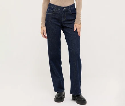Personne portant un jean droit bleu foncé, un haut beige à manches longues avec des détails boutonnés aux poignets et des bottes noires à semelle épaisse.