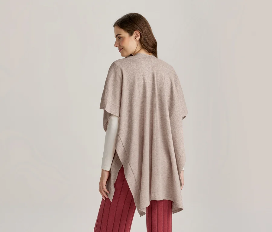 Femme vue de dos, légèrement tournée vers la droite, portant un poncho marron clair sur un haut blanc à manches longues et un pantalon rouge côtelé.