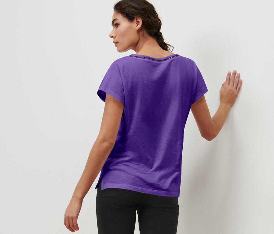 Une femme aux cheveux tressés, vue de dos et appuyée contre un mur, porte un t-shirt en mélange avec modal, violet.