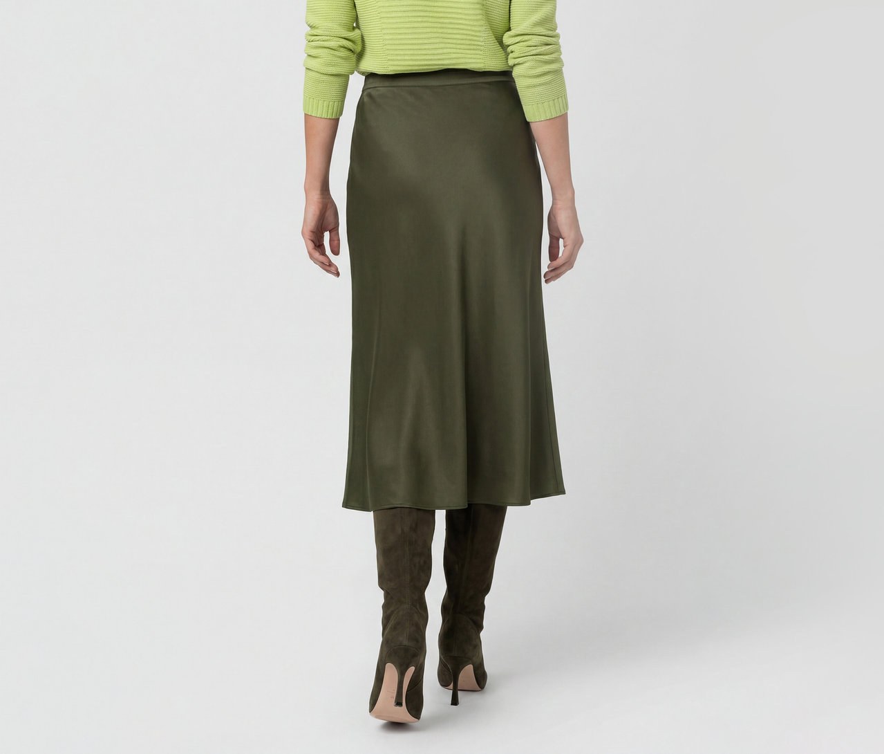 Personne vue de dos portant un pull vert clair, une jupe midi vert foncé et des bottes à talons hauts vert foncé.