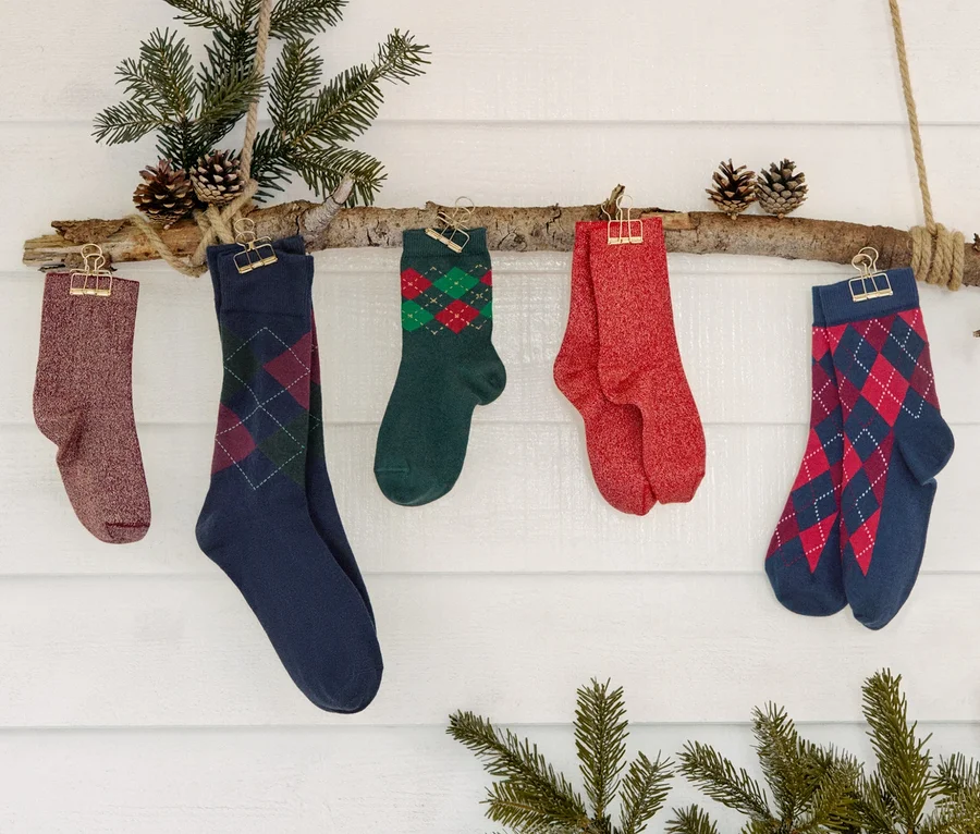 Cinq paires de chaussettes et trois paires de chaussettes scintillantes pour enfants accrochées à une branche décorée de sapin et de pommes de pin.