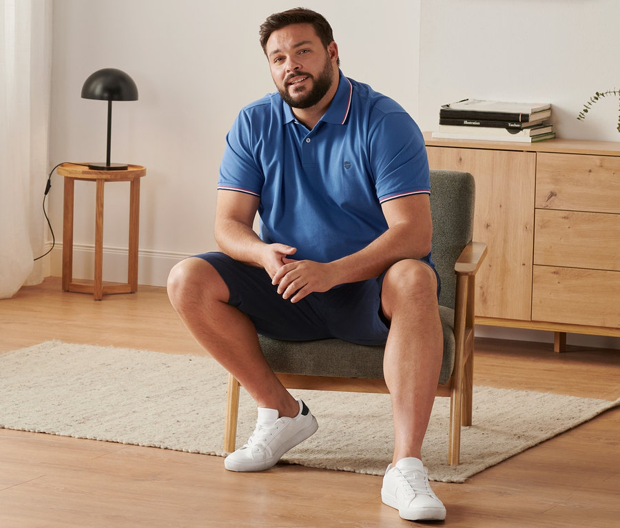 Un homme est assis dans un fauteuil et porte un short chino bleu marine, un polo en piqué bleu roi et des tennis.