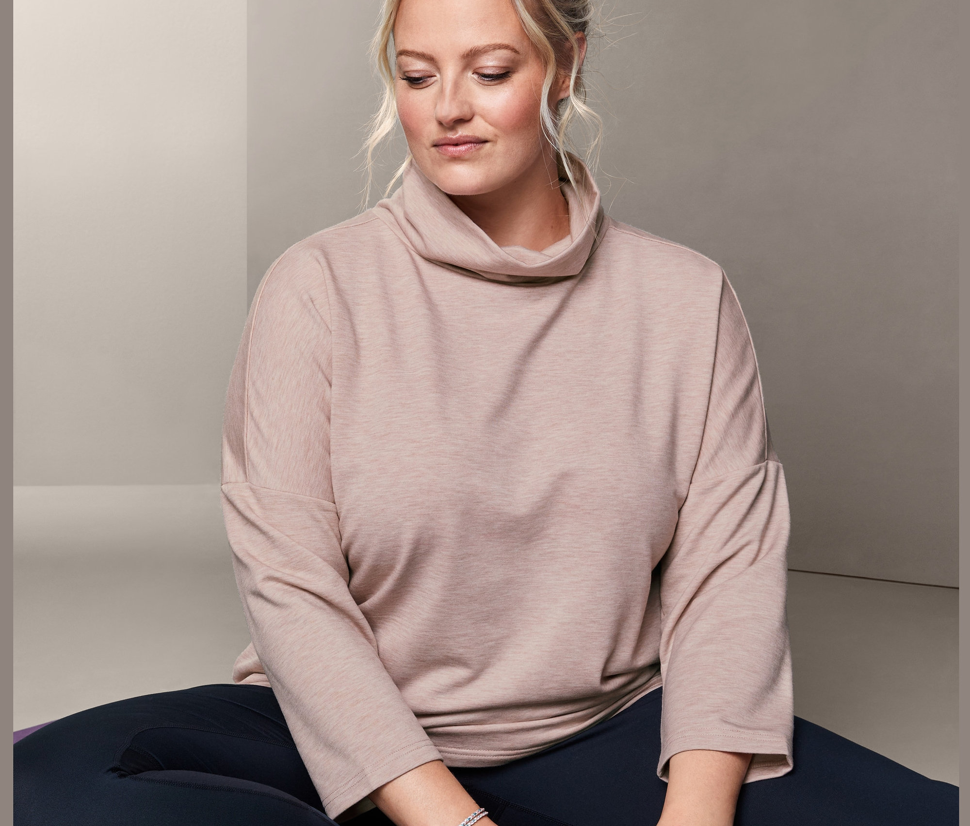 Femme assise sur un tapis de yoga violet portant un pull molletonné.