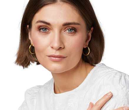 Une femme portant des créoles dorées 23 carats avec pierre synthétique et des créoles dorées avec pierre synthétique.