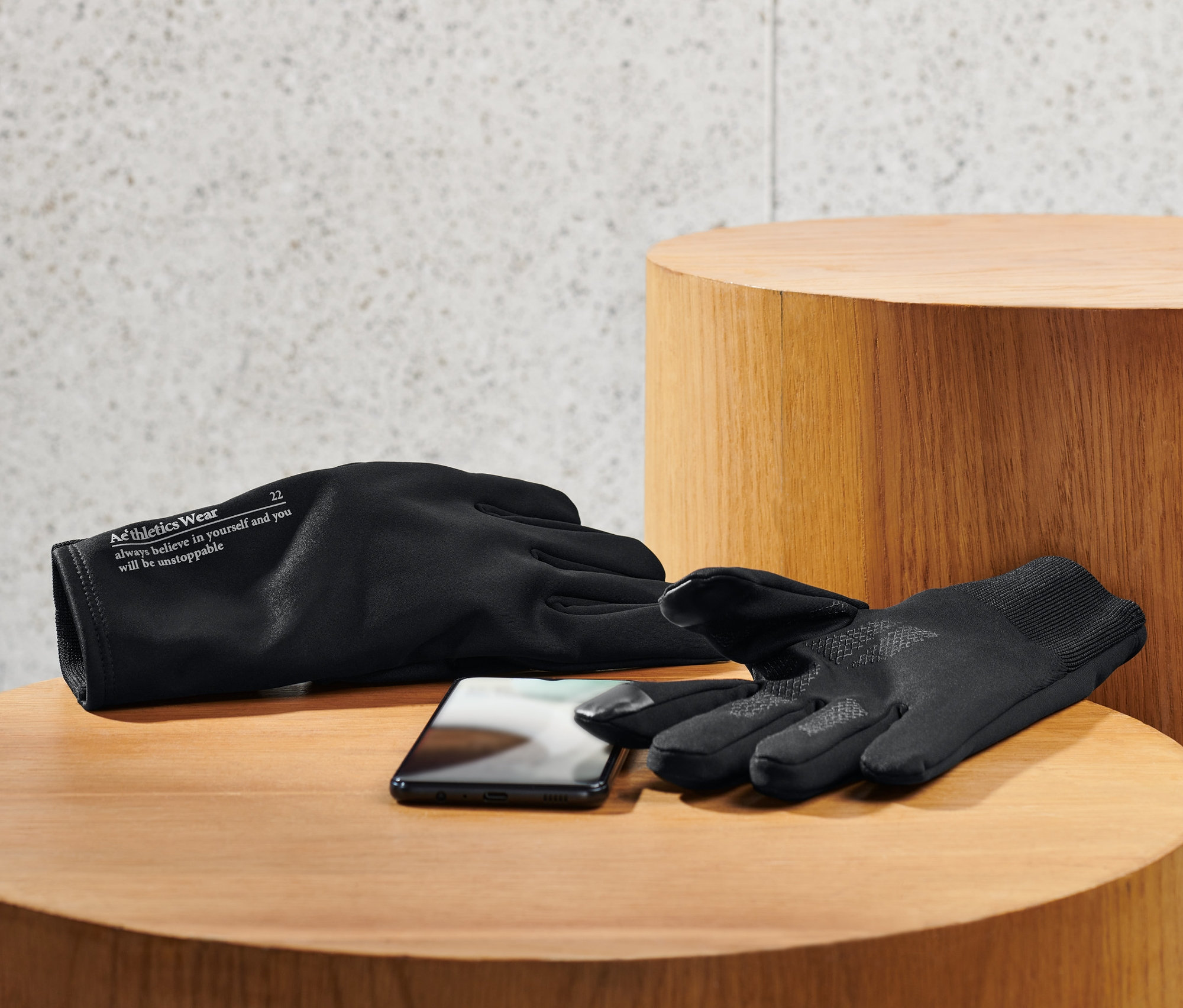 Deux gants coupe-vent noirs et un téléphone portable posés sur une table en bois.
